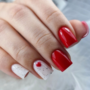 Close-up of beautifully designed Valentine’s Day nails featuring red and white nails with red stipple and red heart design on ring finger