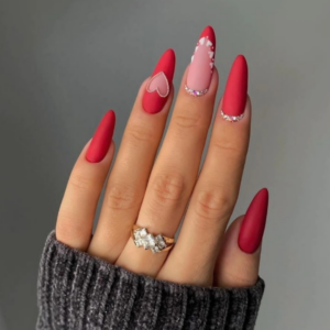 Close-up of beautifully designed Valentine’s Day nails featuring some red nails and one nail with a heart in the middle surrounded by diamonds and one french tips with diamonds