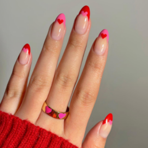 Close-up of beautifully designed Valentine’s Day nails featuring red and pink french tips with heart designs in the middle