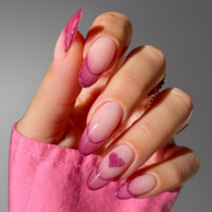 Close-up of beautifully designed Valentine’s Day nails featuring pink outline french tips with glitters and pink glitter heart on ring finger