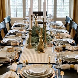 A sophisticated Easter table with a white tablecloth, gold-rimmed plates, gold candle holders, and white roses in a sleek vase.