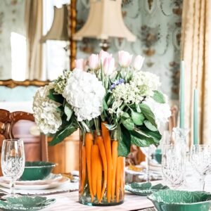 A stunning Easter centerpiece with bright orange carrots in a glass vase, paired with fresh tulips and daffodils for a garden-inspired look.