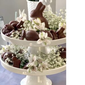 A festive Easter centerpiece featuring a large chocolate bunny surrounded by jelly beans, mini chocolate eggs, and decorative shredded grass.