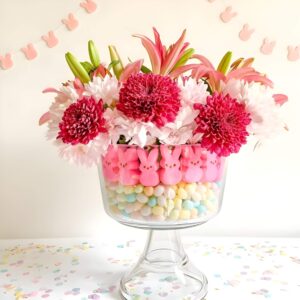 A festive Easter centerpiece using a glass jar layered with colorful jelly beans, pastel M&Ms, and chocolate eggs, topped with fresh flowers.