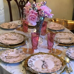 A vintage Easter table with lace tablecloths, delicate china, antique silverware, mismatched teacups, and pastel roses.