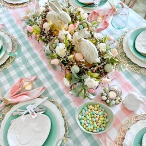 A sleek and modern Easter table with neutral-toned dinnerware, linen napkins, white candles, and a simple floral centerpiece. 